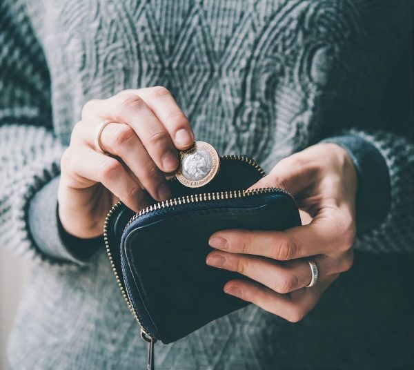 Hands holding british pound coin and small money pouch
